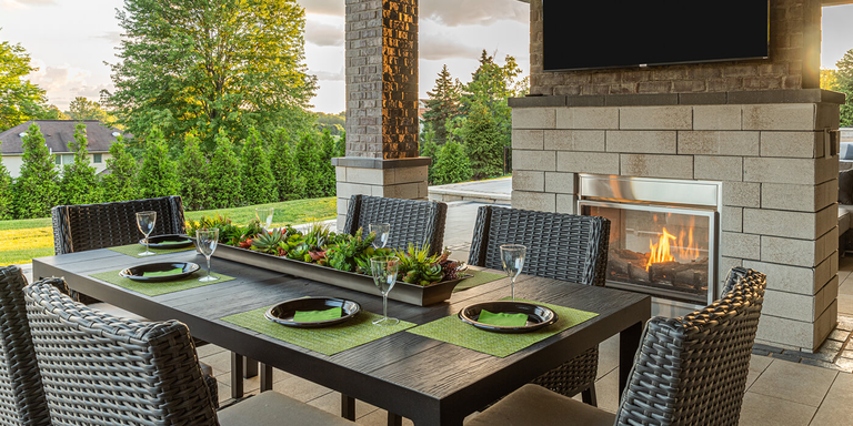 An outdoor dining and living room space with a see-through gas fireplace installed under a TV