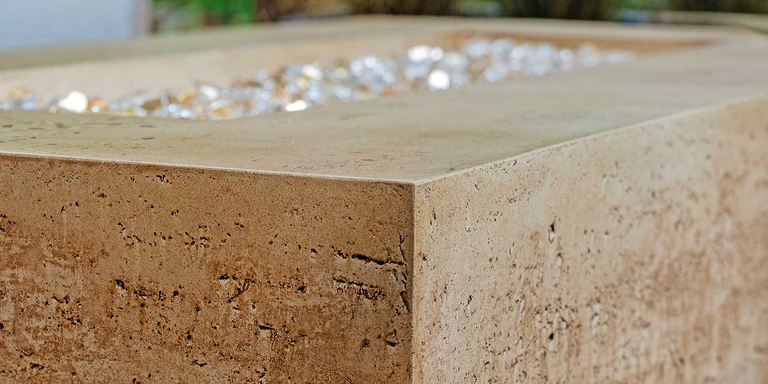A close-up of the Tuscan Gas Fire Pit by FlameCraft, showing its Travertine-style finish
