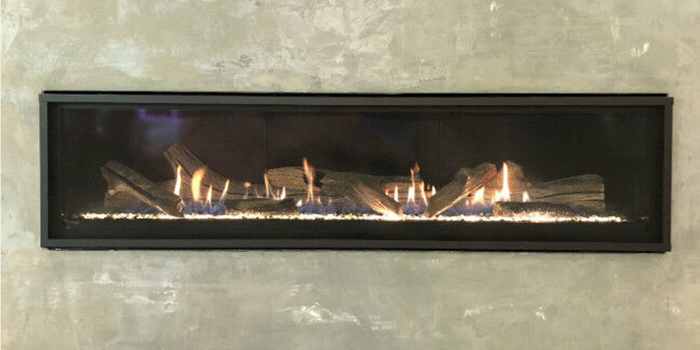 Black linear fireplace with glowing fire, crystal fire glass, and driftwood logs in a cement hearth