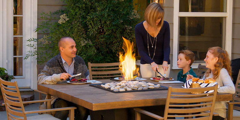 A family sitting around an outdoor gas fire pit dining table 