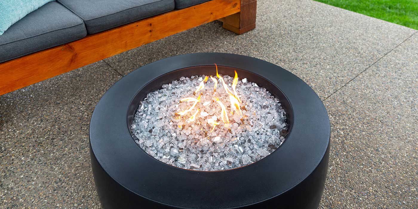 A small, low-profile fire pit with clear fire glass media on an outdoor patio.