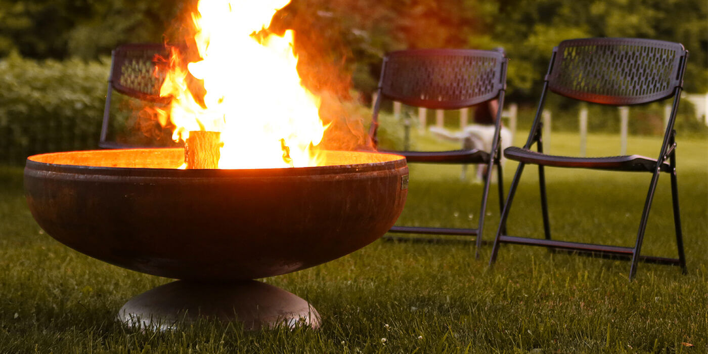A large wood burning fire pit set up next to two lawn chairs