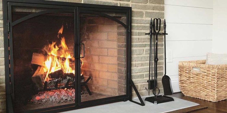 A wood burning fireplace with a screen and a black cast iron fireplace tool set