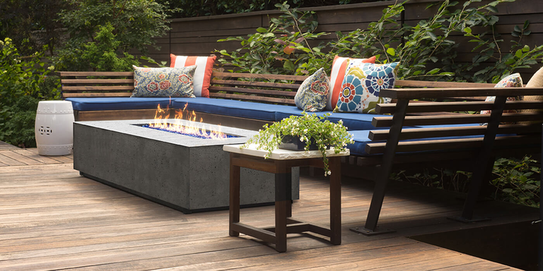 An outdoor lounge space with built-in bench seating around a linear concrete gas fire pit