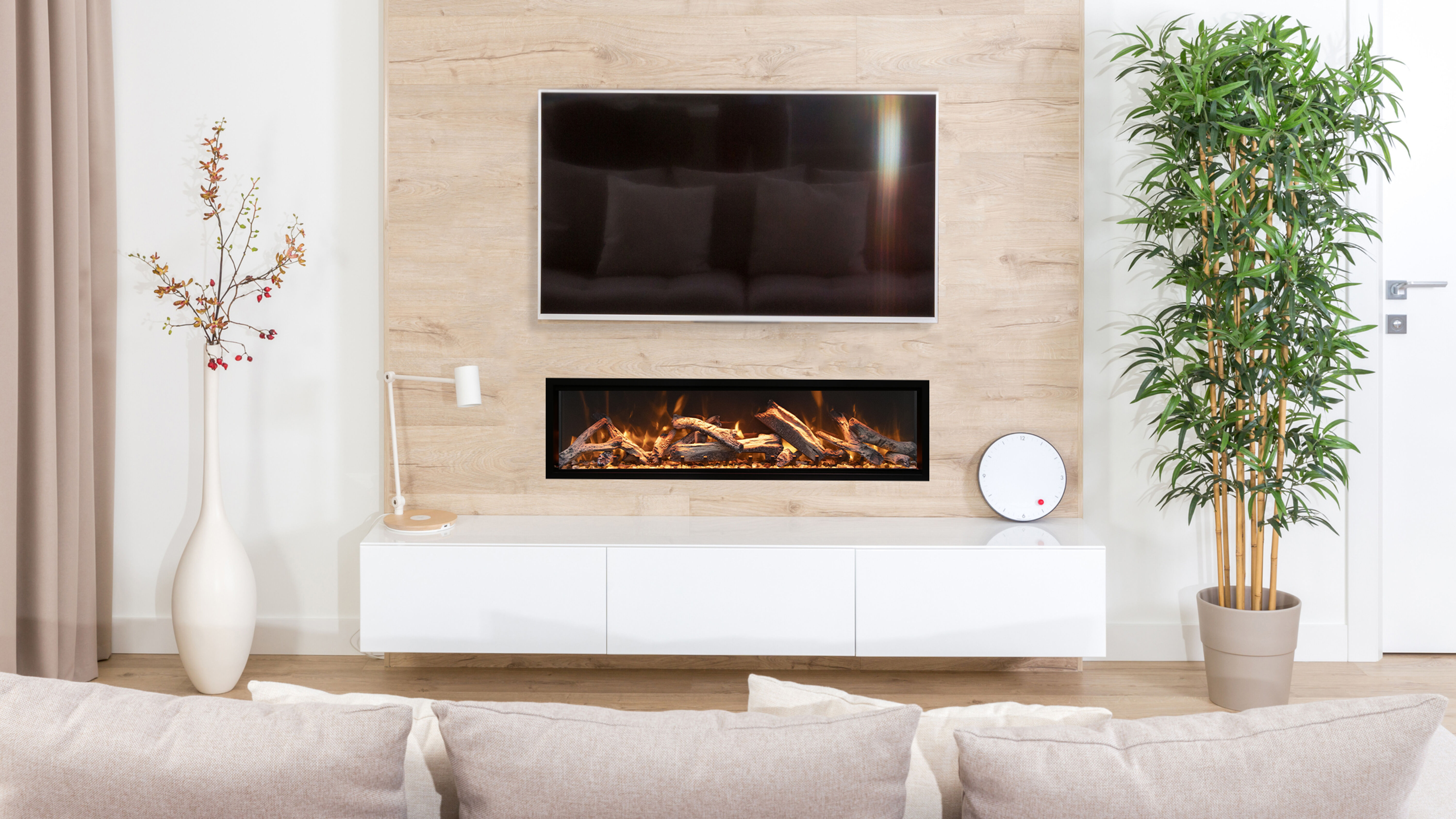 A modern living room with neutral-colored furniture, white walls, a tall floor plant, a linear gas fireplace, and a flatscreen TV.