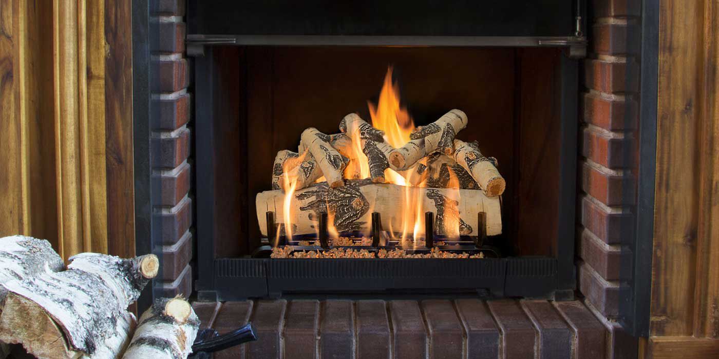 A traditional, brick fireplace hearth with a birch wood style gas log set