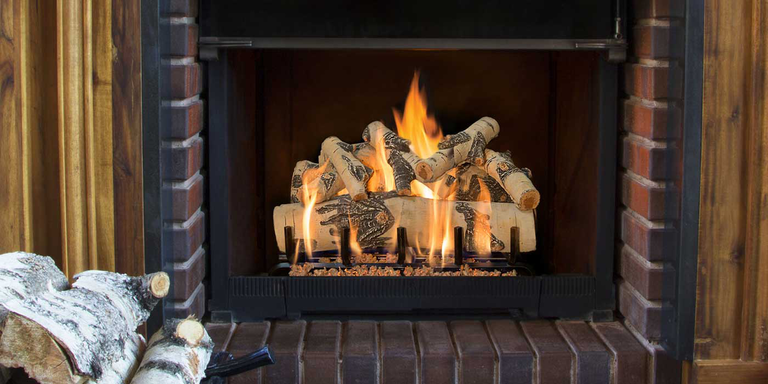 A traditional, brick fireplace hearth with a birch wood style gas log set
