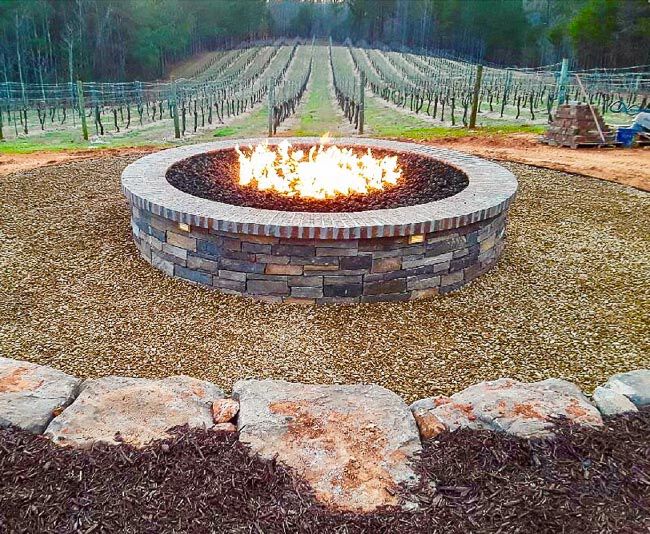 Large masonry fire pit burning in front of a vineyard