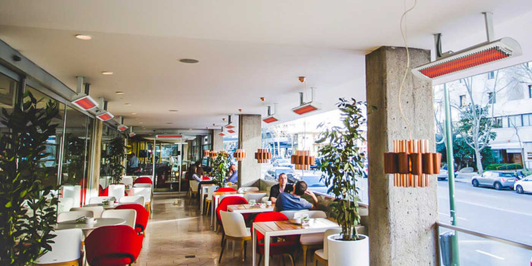 An semi-enclosed restaurant patio space with several patio heaters mounted above the tables