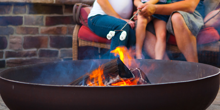 A family of three roasting marshmallows over a wood burning fire pit in their backyard