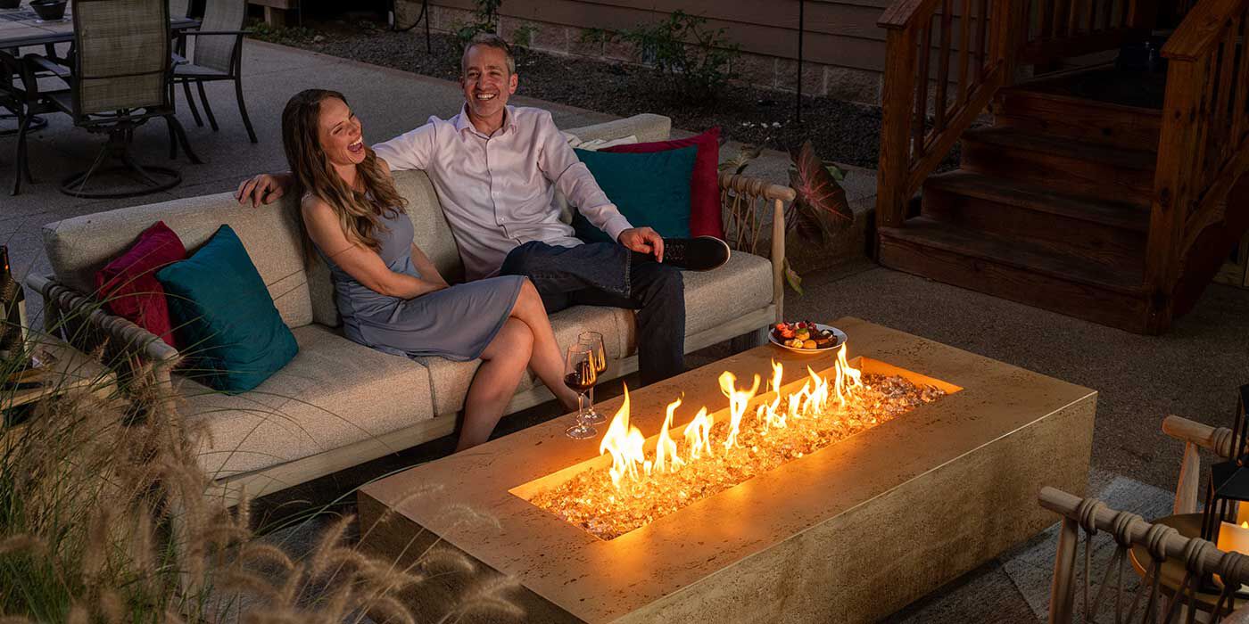 A couple sitting next to a Tuscan Gas Fire Pit by FlameCraft at night