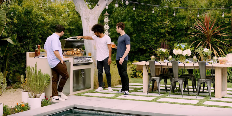 Three men standing outside around a grill installed in a custom outdoor kitchen island near an outdoor dining table