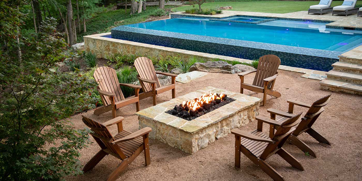 An outdoor seating area next to pool with six chairs and a natural stone gas fire pit 