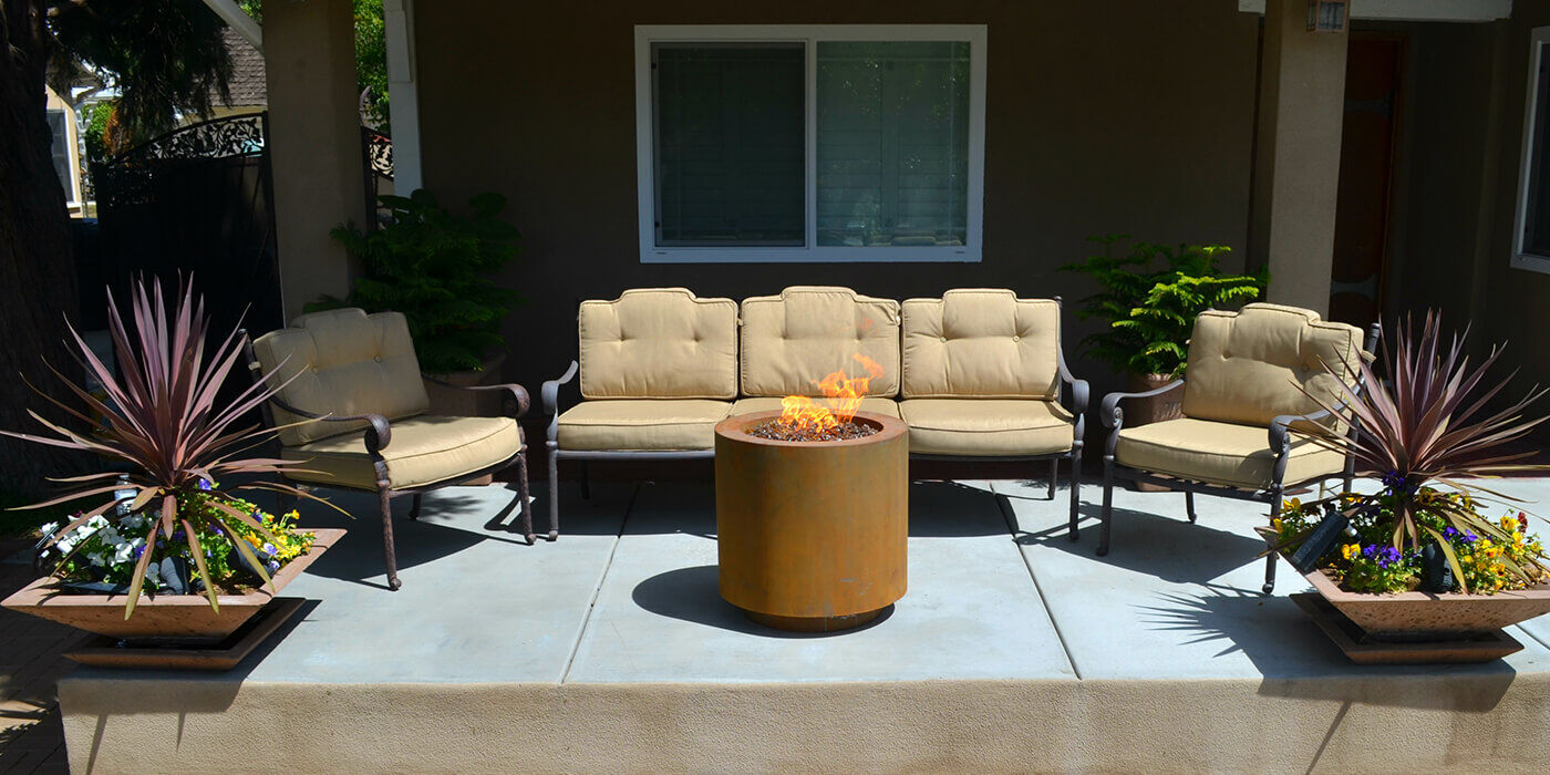 An outdoor patio space with a small, round Corten steel gas fire pit An outdoor patio space with a small, round Corten steel gas fire pit