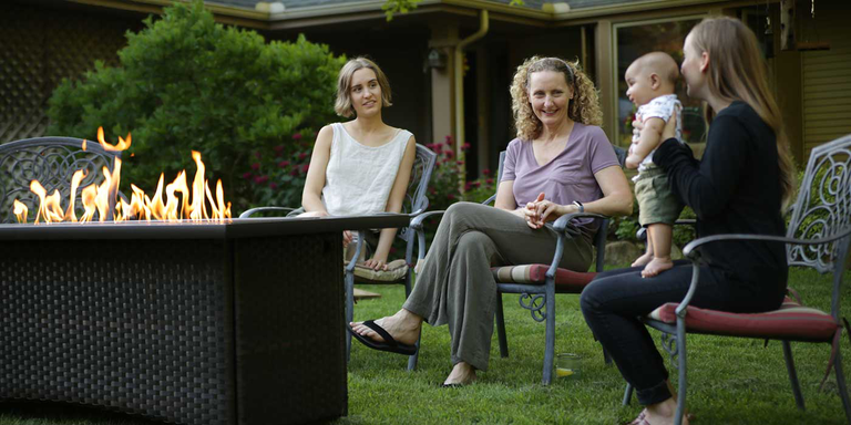 A group of women and a baby sitting next to a coffee-table-height gas fire pit table 