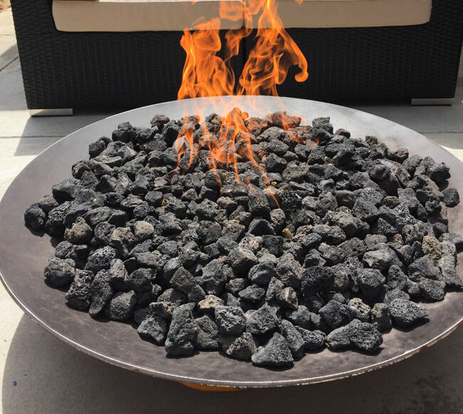 Flames flickering above black lava rocks in a round metal fire pit