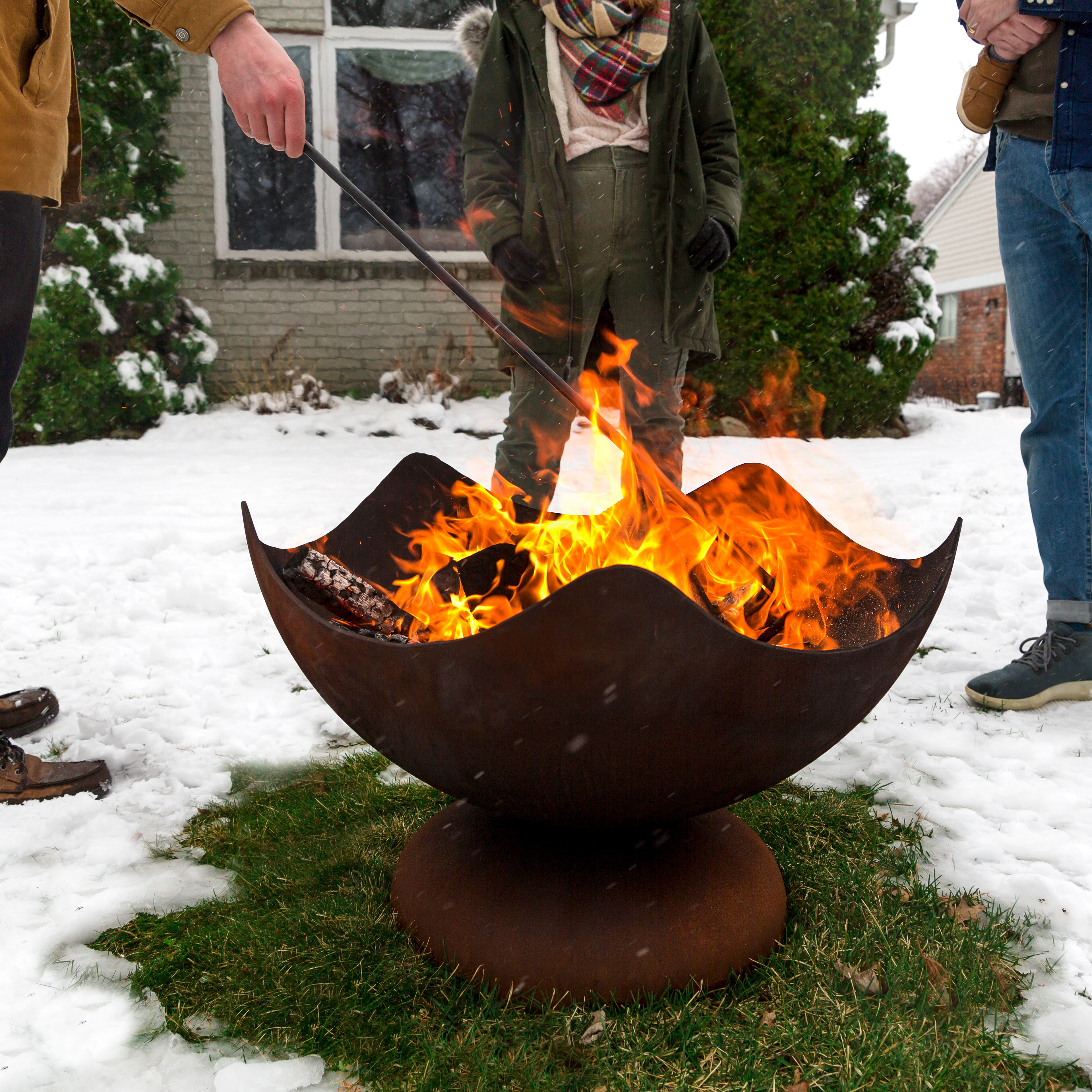 Man holding a black steel fire pit poker next to a Stellar Fire Pit