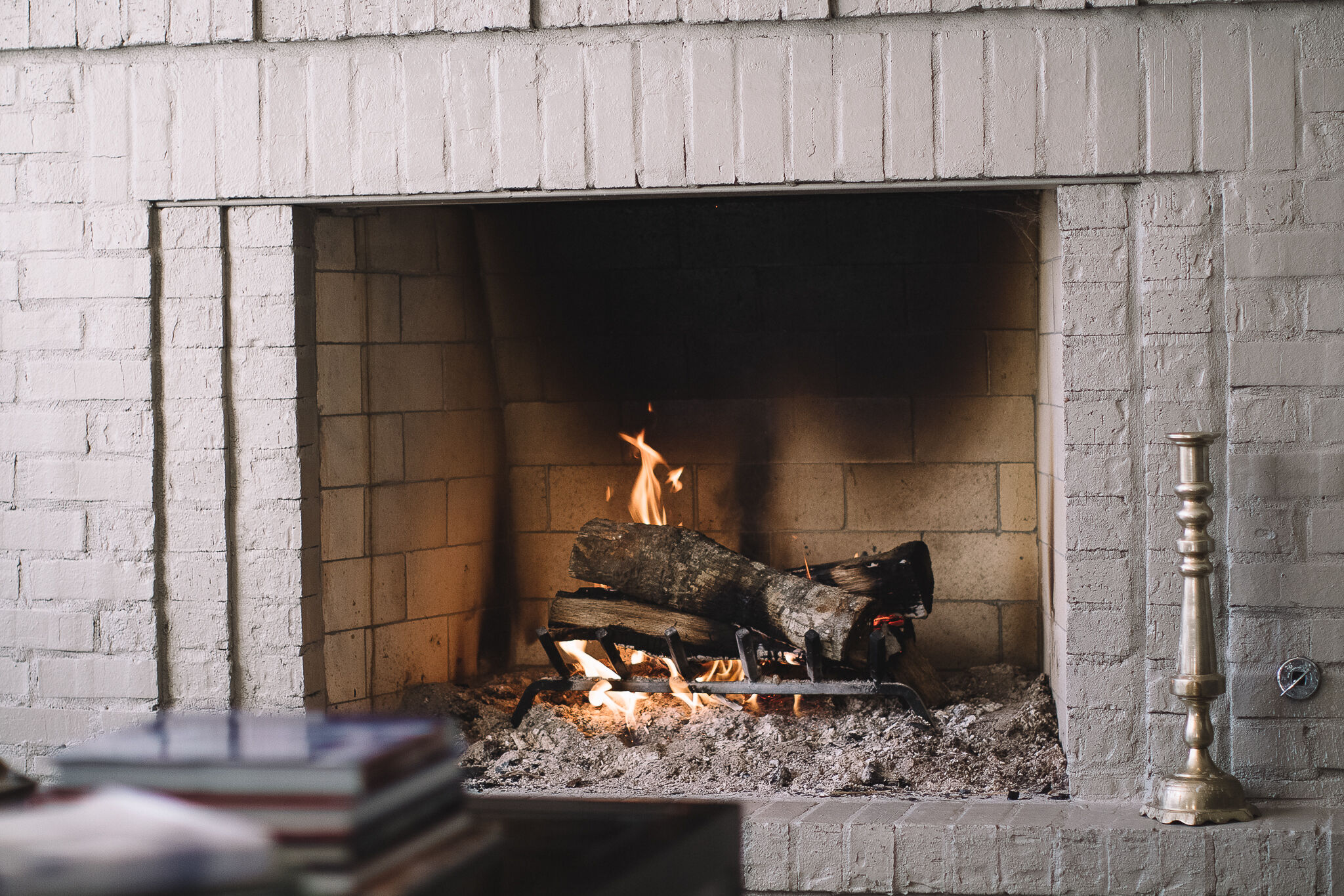 A close-up view of a masonry, wood burning fireplace with a traditional black grate and burning logs.