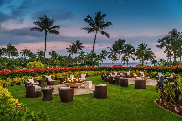 Gas fire pits surrounded by chairs at a Hawaiian resort during sunset