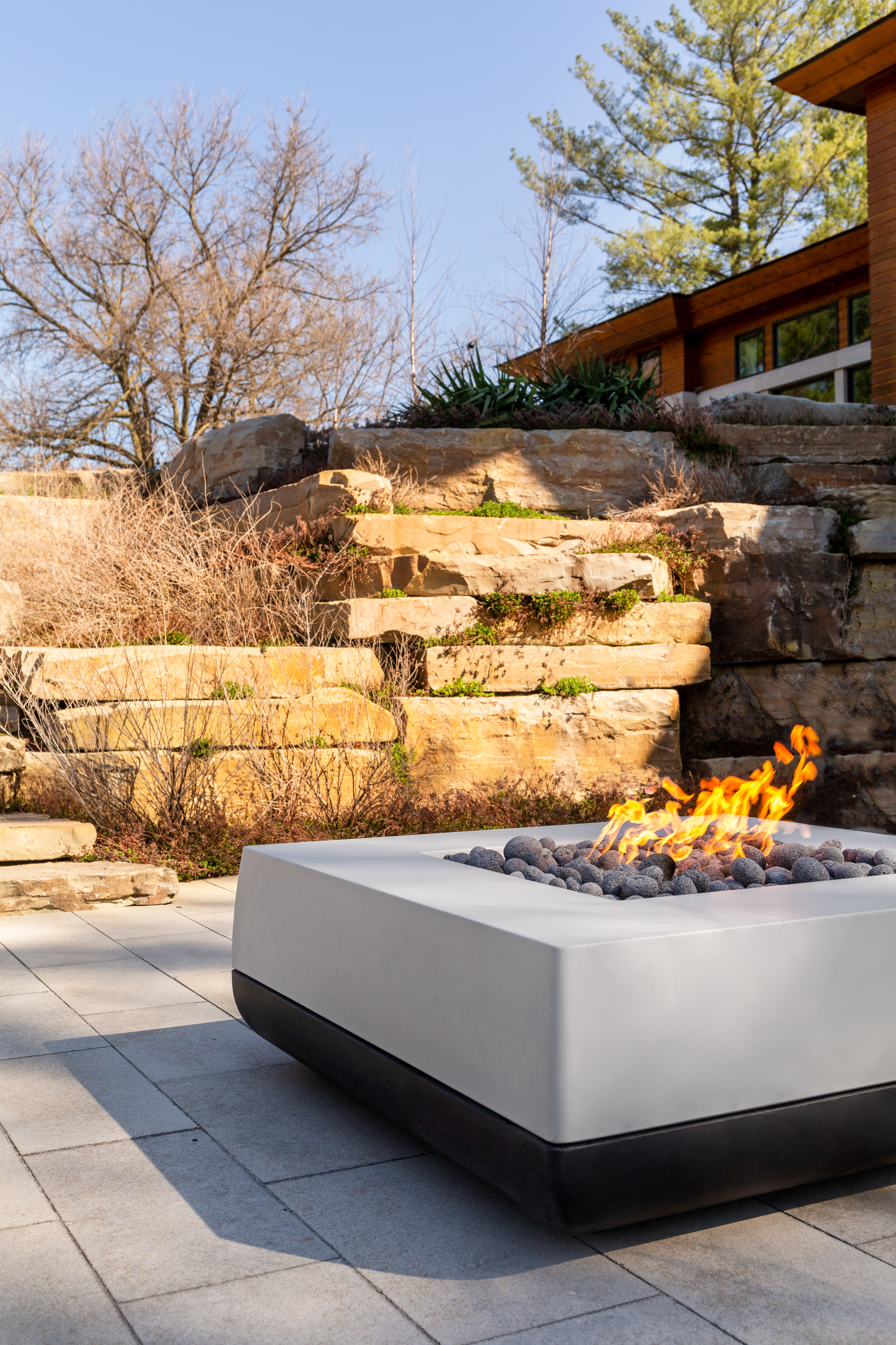 An outdoor space with a 48-inch, square, gray and black Quadro gas fire pit from FlameCraft.