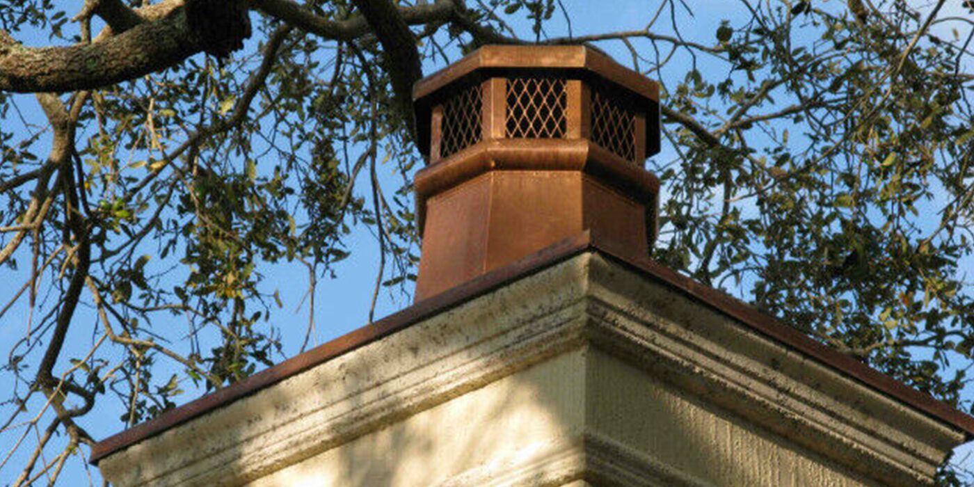 Copper chimney cap on a masonry chimney with trees hanging overhead
