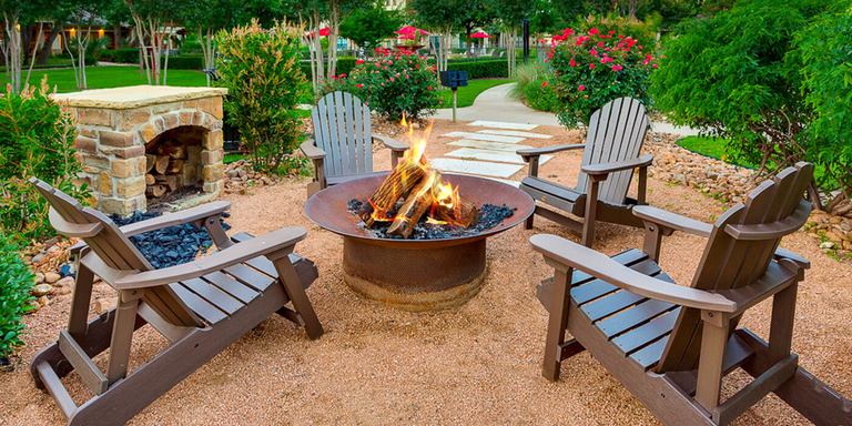 A wood burning fire pit in an outdoor garden area with Adirondack chairs 