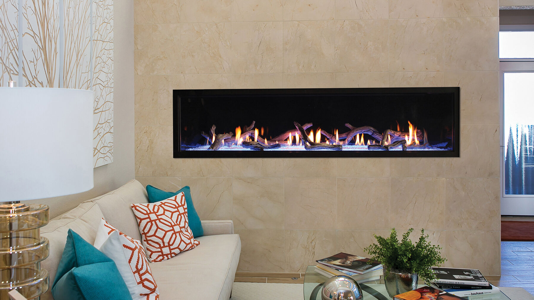 A contemporary living space with beige walls, a massive linear gas fireplace, and a white couch with blue, orange, and white accent pillows. 