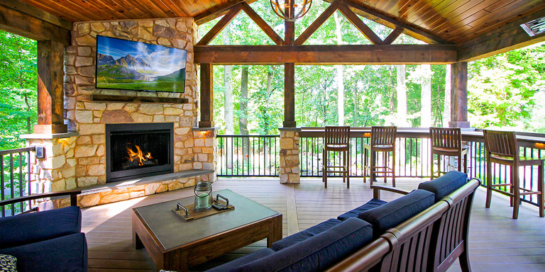 A covered outdoor patio space with bar seating and a lounge area with a couch, chair, coffee table, fireplace, and mounted TV