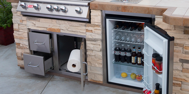 An outdoor kitchen island with a fridge, storage drawers, side burner, and grill head