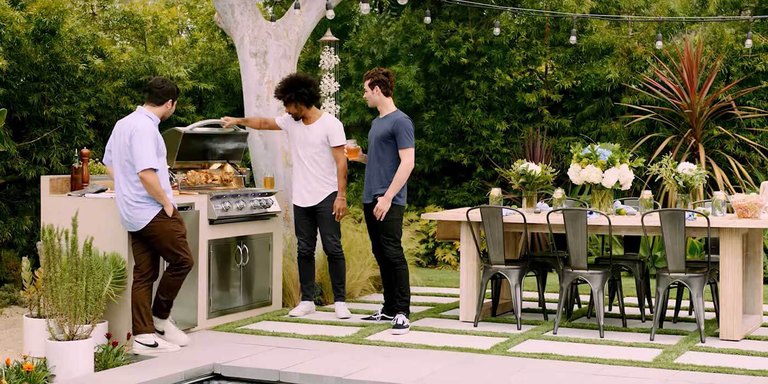 A backyard deck with a pool, a dining table and chairs, and a large gas cart-mount grill from American Made Grills.