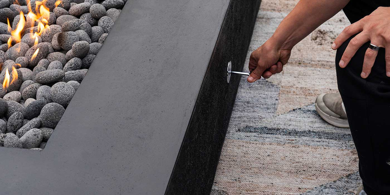 A close-up of a person turning a match-lit gas fire pit ignition key