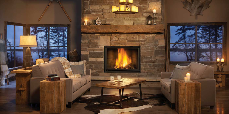 A traditional living room with shiny, dark hardwood flooring, a plush, beige couch, built-in shelves with photos, an ornate, white side table, and a large hearth with a white mantel and a black wood burning fireplace.