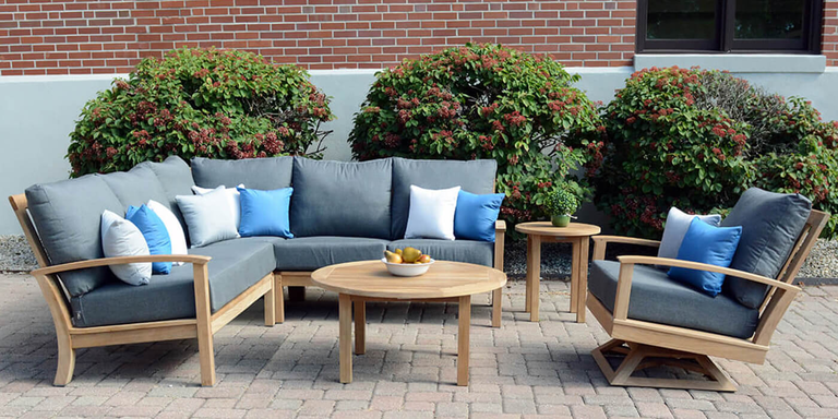 An outdoor sofa, chair, and coffee table made of durable teak and complete with light gray cushions.