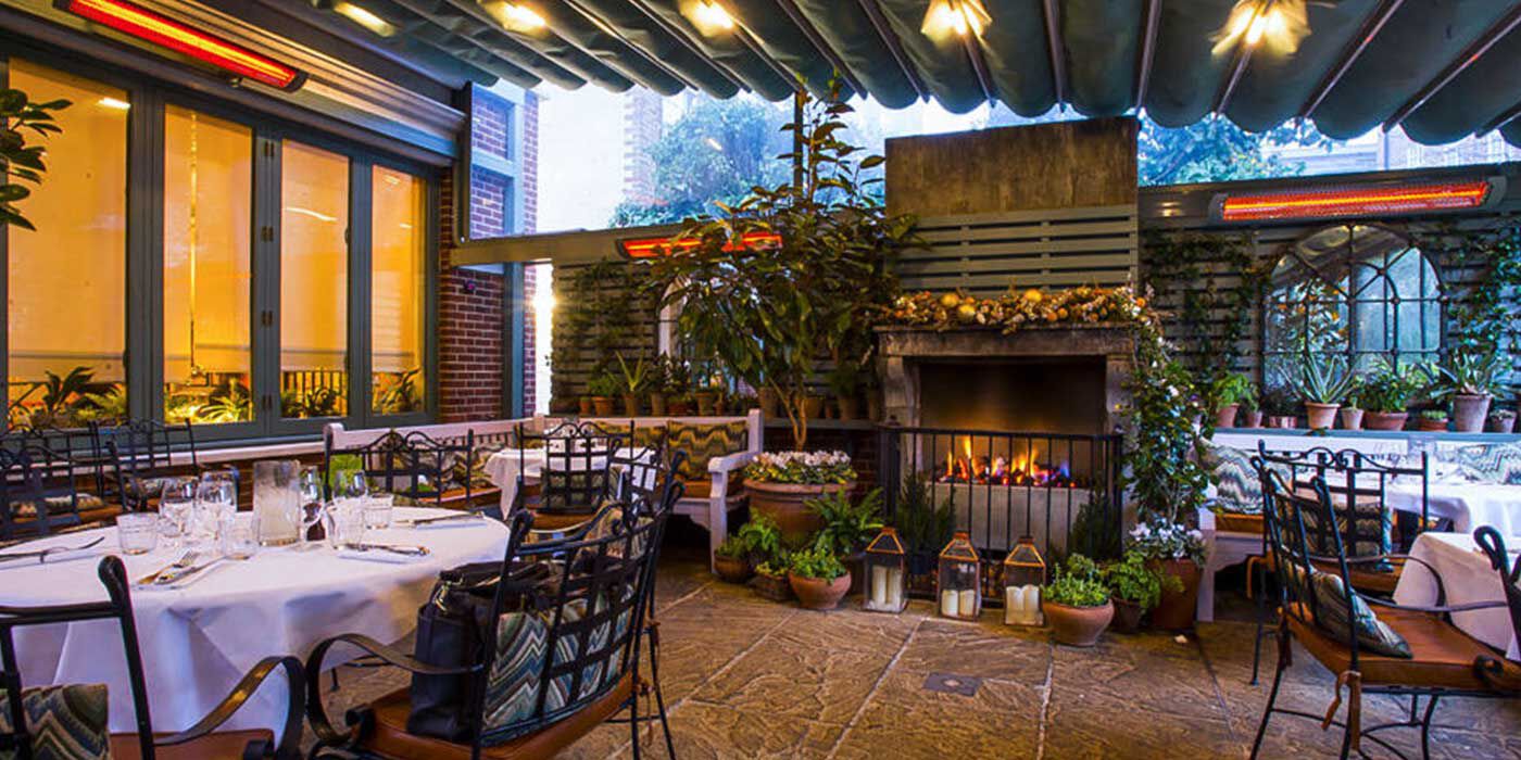 An outdoor restaurant patio space with several patio heaters installed above the tables and a large outdoor fireplace 