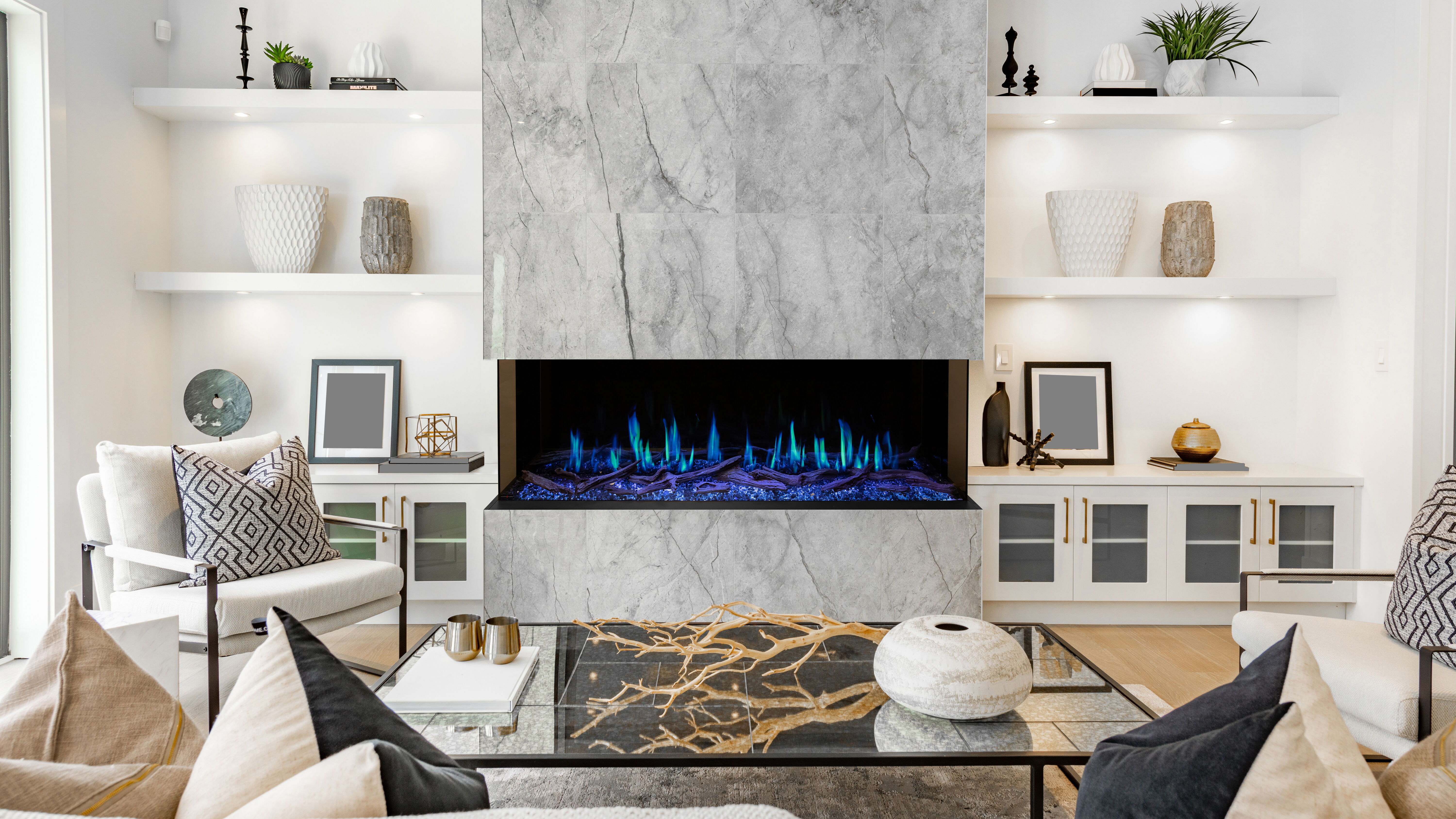 A modern living room with built-in shelving and a large electric fireplace that has blue flames and accent lighting.