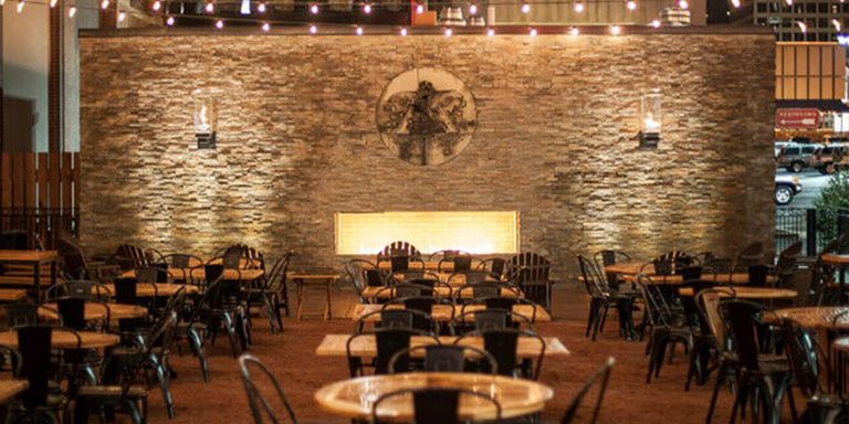 Outdoor patio with tables and chairs in front of a large stone wall with a fireplace in the middle