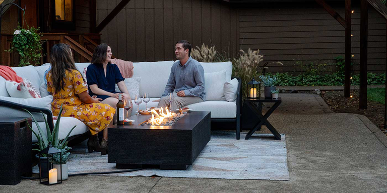 A FlameCraft Zen gas fire pit installed on an outdoor patio with two couples sitting nearby on an outdoor sofa