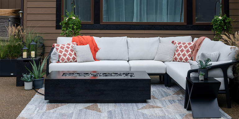 The FlameCraft Zen Gas Fire Pit with a large white outdoor sofa and two black side tables