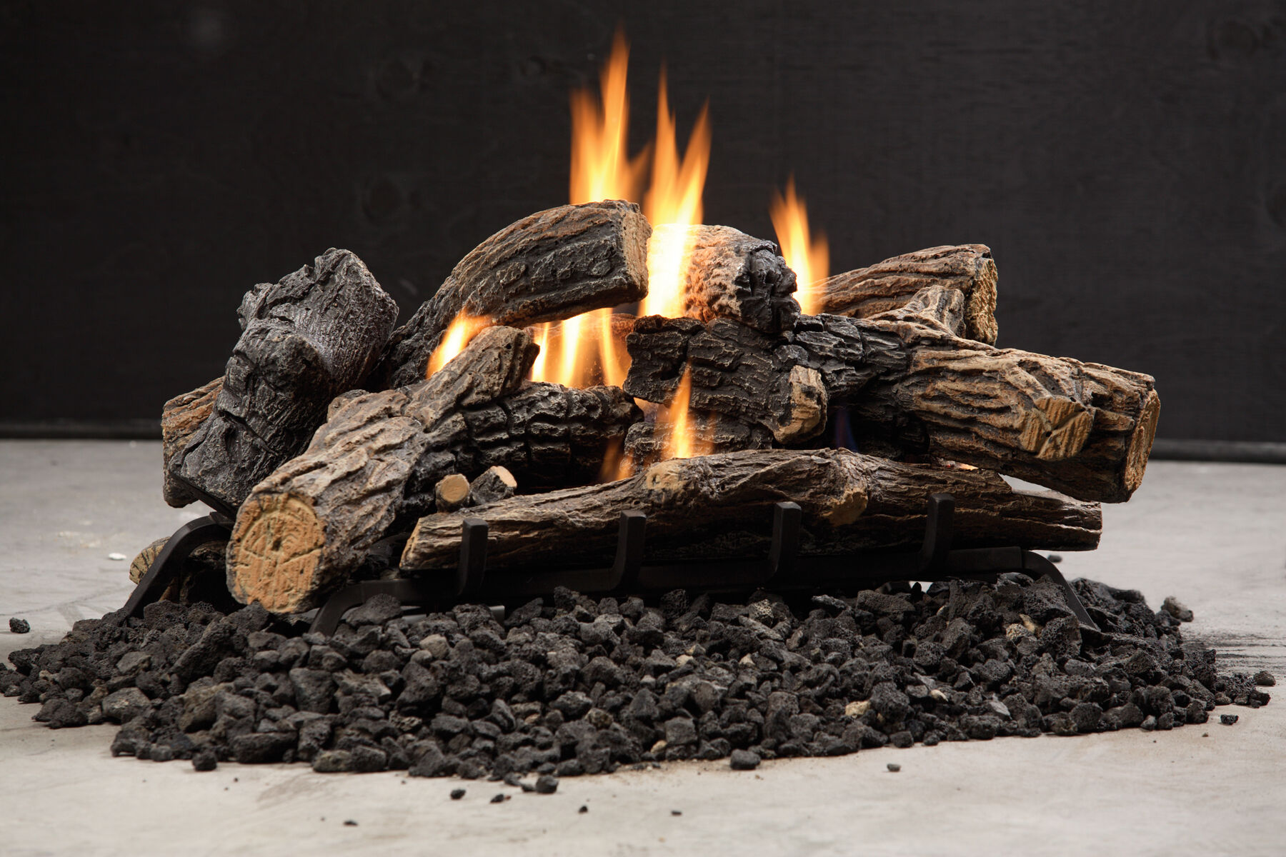 A gas log set with textured brown-gray bark, black lava rock, and orange flames.