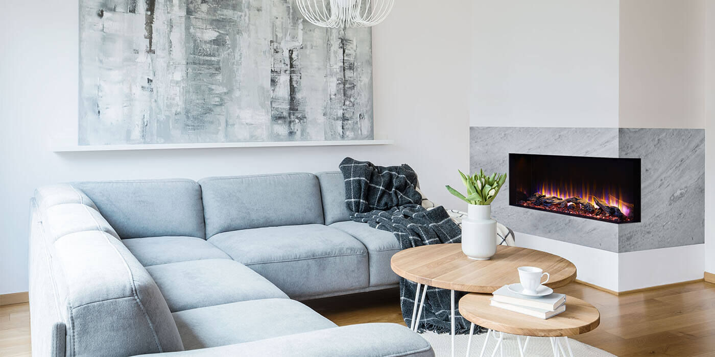 A modern living room with a large blue sectional couch and a two-sided electric fireplace built into the corner of a wall