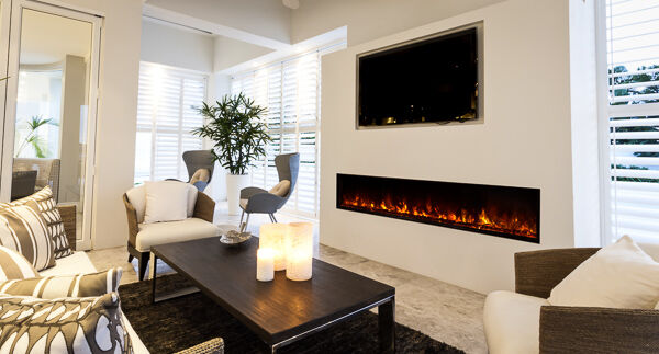 A modern living room with white walls, a large, linear fireplace with orange flames, a flatscreen TV above the fireplace, and modern, white and grey furniture.