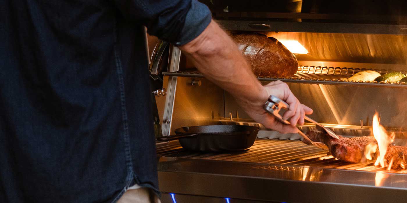 A man putting a steak on flaming, stainless steel grill grates at night.