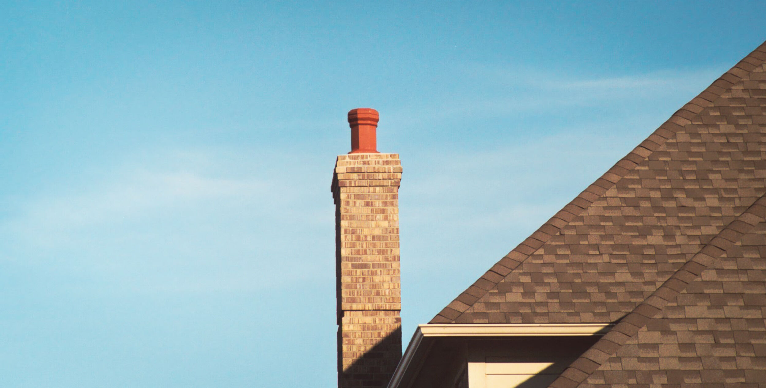 A rooftop with a single masonry chimney stack that's topped with a brown clay chimney cap.