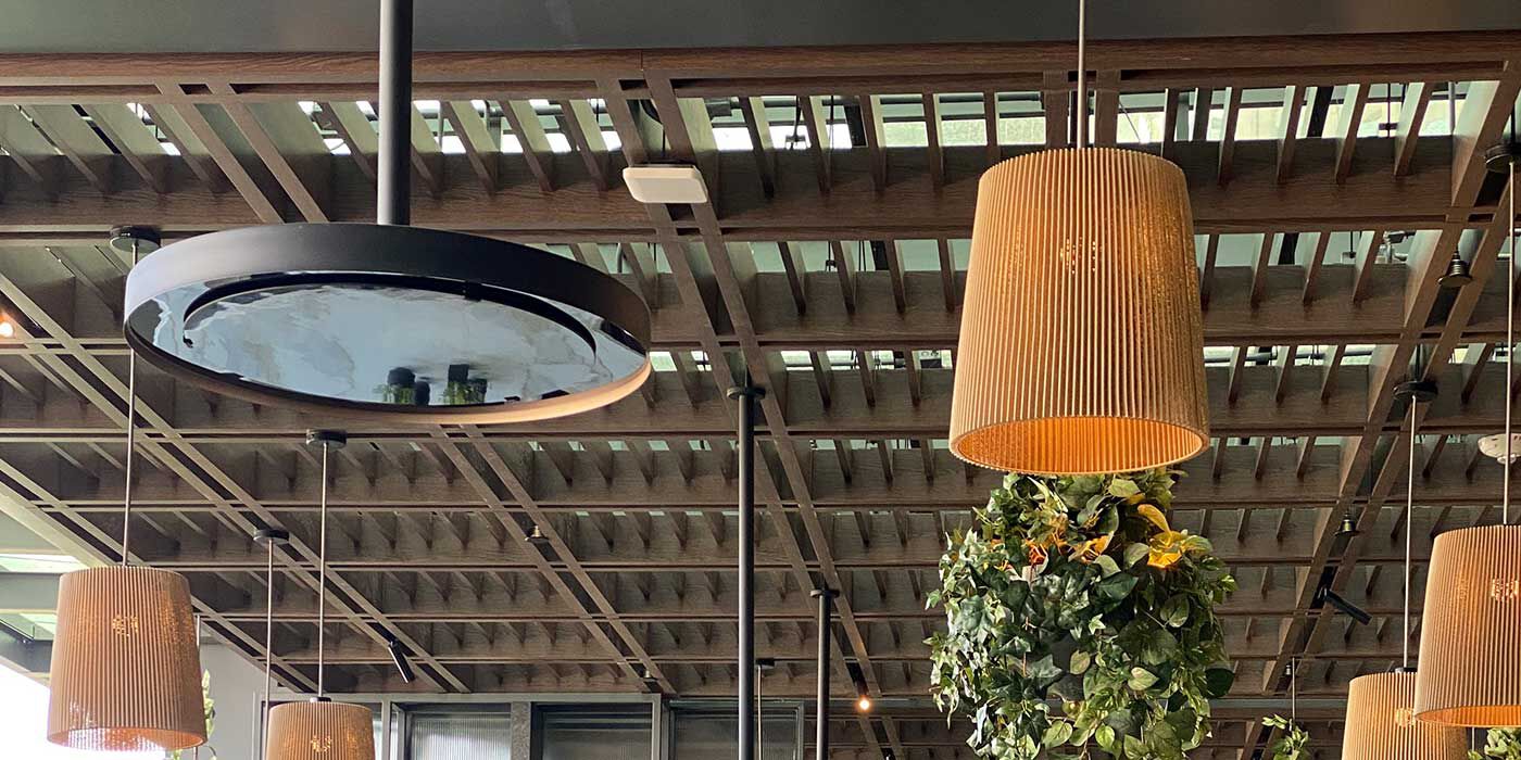 An outdoor restaurant patio with two tables, red chairs, greenery and fairy lights on the ceiling, and two overhead gas patio heaters.