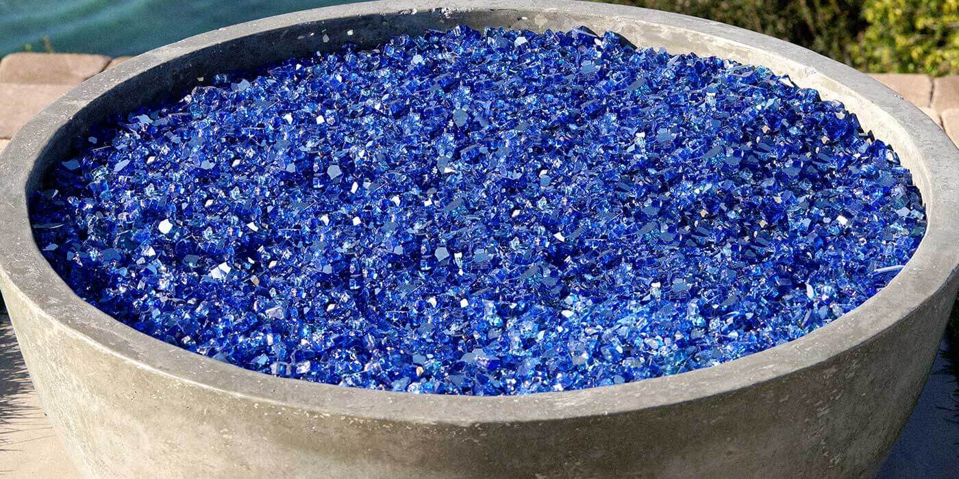 A close-up view of a small, concrete gas fire bowl with blue accent fire glass media.