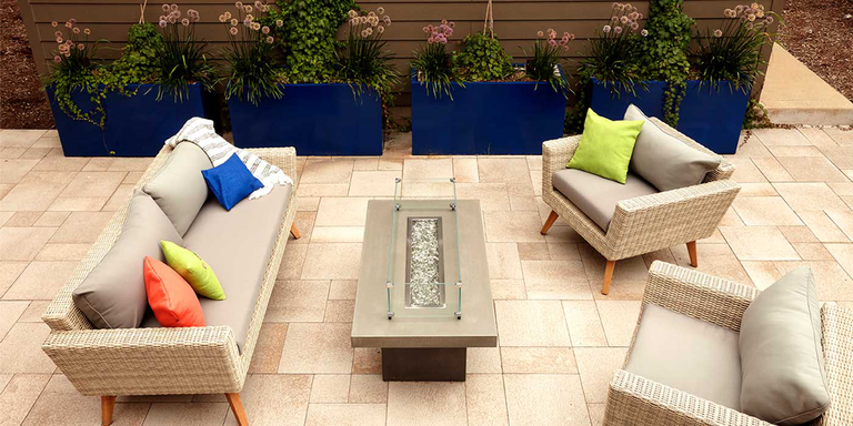 An outdoor patio with two chairs, a sofa, and an linear gas fire pit with a burn from Firegear