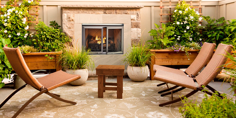 An outdoor space with chairs, a table, plants, and an outdoor fireplace with stainless steel doors