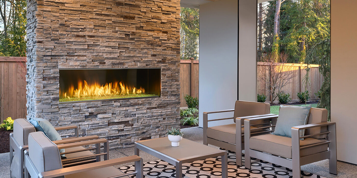 A tropical outdoor space with a blue, customized outdoor cooking area and a built-in outdoor-rated gas fireplace.
