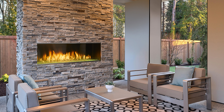 A tropical outdoor space with a blue, customized outdoor cooking area and a built-in outdoor-rated gas fireplace.