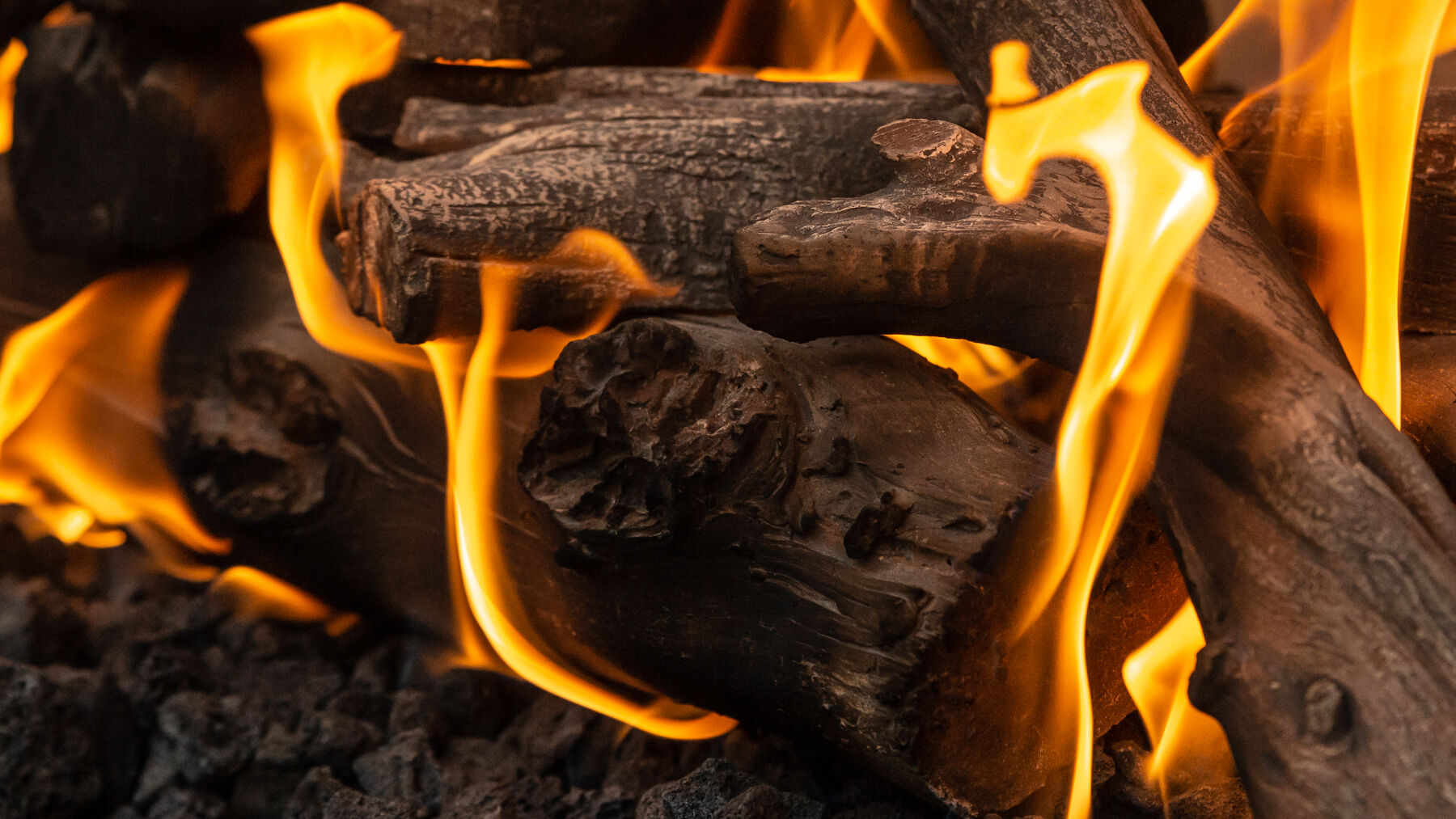 A close-up view of a rustic gas log set with hand-painted bark details and orange flames.